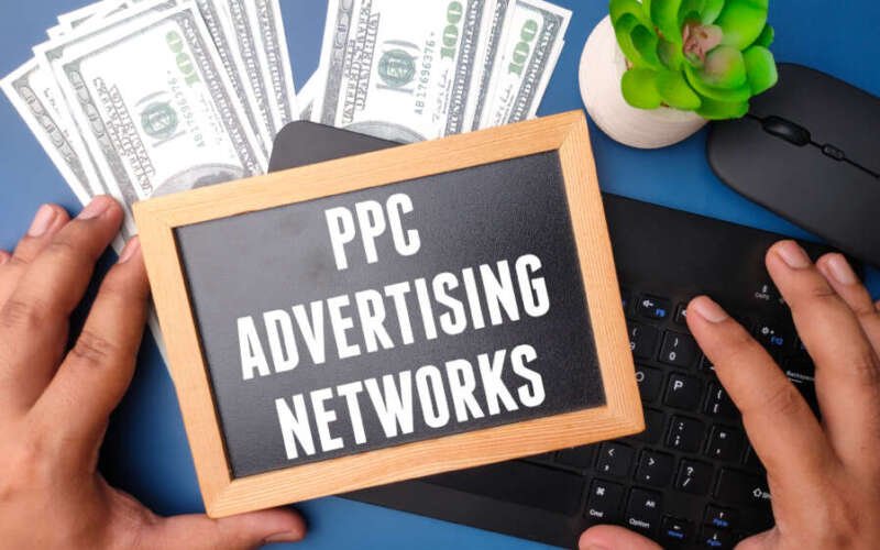 Banknotes,wireless keyboard and black board with text PPC ADVERTISING NETWORK on blue background.