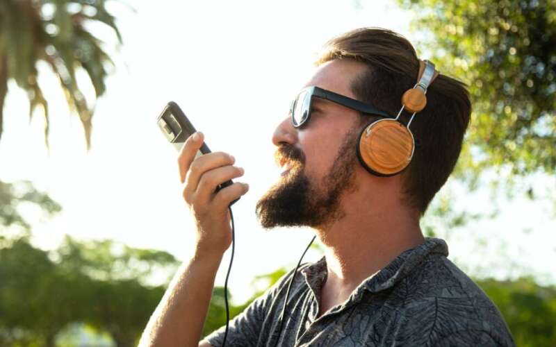 Side view of caucasian male recording voice message using mobile phone outdoors.